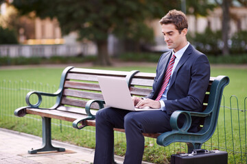 Fototapeta premium Businessman, laptop and typing on park bench in nature for trading, checking email or outdoor networking. Man or trader in business suit on computer for communication or finance on outside furniture