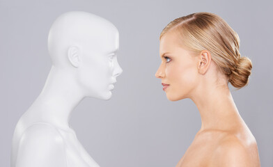 Studio, woman and mannequin with beauty clone versus artificial standard, perfect and facial wellness. Girl, doll and face in profile for cosmetics, plastic surgery or makeup on grey background.