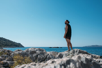 A male tourist is relaxing on a rocky coast on a hot day.