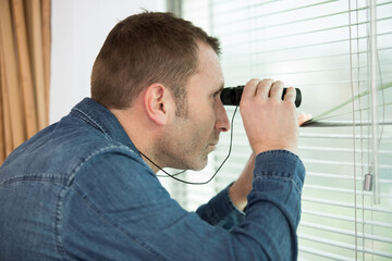 man watching out the window with binoculars - obrazy, fototapety, plakaty