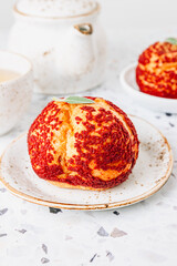 Small cakes profiterole choux pastry with custard, strawberry jam and red icing on a white concrete background.