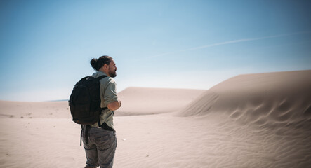 A young male tourist walks through the desert sands to the sea.