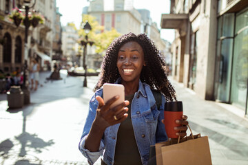 Happy young woman with shopping bags using smartphone in city