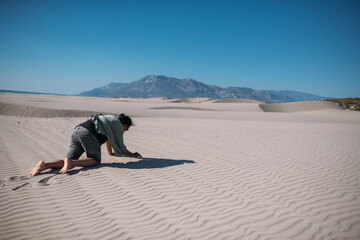 An emaciated man crawls under the scorching sun on the sand in the desert.