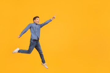 Fototapeta na wymiar Look At This. Teen boy pointing aside while jumping up in air