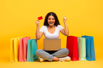 Emotional young indian lady with laptop and credit card