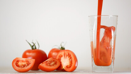 Delicious tomato juice is poured in jug next to tomatoes on the background 