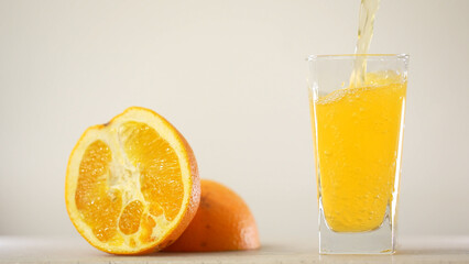 Detail Shot of Pouring Fresh Orange Juice into Glass. Appetizing orange juice swirls into a wave in a glass against the background of cut oranges.