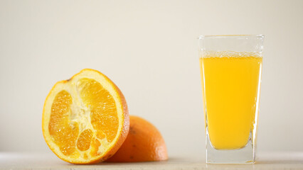 Detail Shot of Pouring Fresh Orange Juice into Glass. Appetizing orange juice swirls into a wave in a glass against the background of cut oranges.