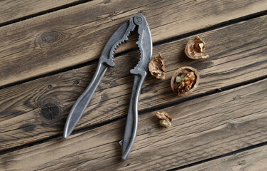 A chopped walnut against a wood grain background next to a nutcracker.