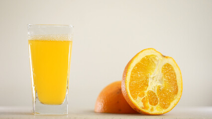 Detail Shot of Pouring Fresh Orange Juice into Glass. Appetizing orange juice swirls into a wave in a glass against the background of cut oranges.
