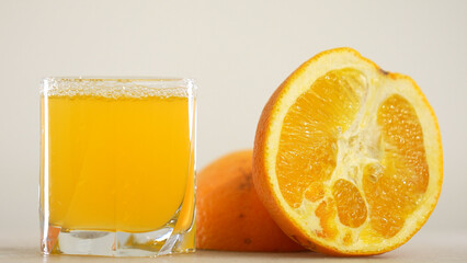 Detail Shot of Pouring Fresh Orange Juice into Glass. Appetizing orange juice swirls into a wave in a glass against the background of cut oranges.