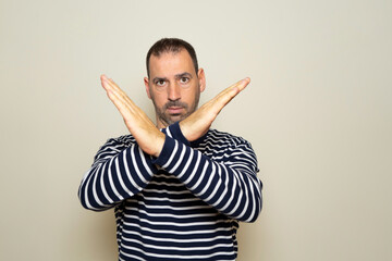 Portrait of serious Hispanic man with hands crossed, showing x sign which means stop, warning of...