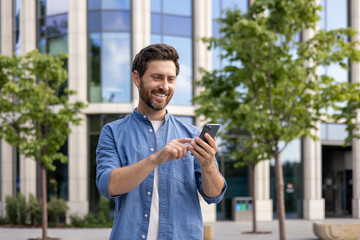 Bearded businessman smiling while using smartphone outside modern office building