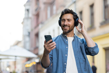 Bearded mature man enjoying music on headphones while using smartphone in city