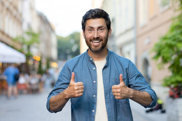 Cheerful bearded man giving thumbs up walking in evening city street