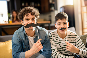 Dad and son holding fake mustache. Prostate cancer prevention