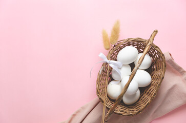 A basket with Easter eggs and spikelets on pink background, top view and copy space.