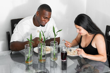 young latin multiethnic couple, eating pasta sitting in the dining room while conversing