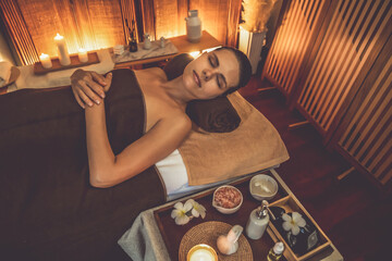 Fototapeta na wymiar Caucasian woman customer enjoying relaxing anti-stress spa massage and pampering with beauty skin recreation leisure in warm candle lighting ambient salon spa at luxury resort or hotel. Quiescent