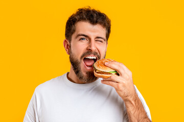 Funny eater guy biting burger winking eye at camera, studio