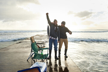 Happy, portrait and people fishing at ocean with pride for tuna catch on pier at sunset. Fisherman, friends and smile holding fish in hand with success in nature at sea on holiday or vacation