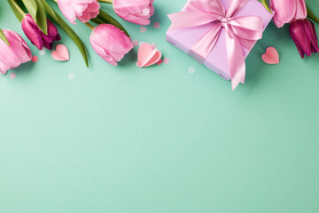 Mother's Day gift ideas: sentiments in spring hues. Top view shot of a gift box amid tulips, hearts on teal background with space for heartfelt greetings