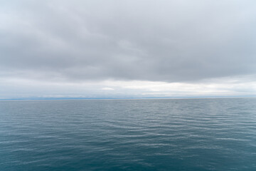 View of serene sea waves from a ship, emerald water, and overcast weather.