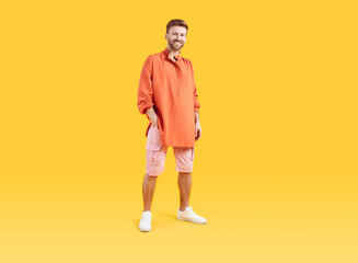 Full body photo of young happy man standing with one hand in pocket wearing summer casual clothes and white sneakers isolated on yellow studio background. Portrait of smiling guy looking at camera.