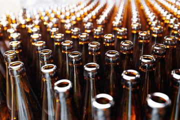 Glass bottles of beer on dark background with sun light. Concept brewery plant production line.