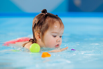 Fototapeta na wymiar Happy baby girl swims and plays with balls in pool with trainer. Concept developing fine motor skills and health care of child