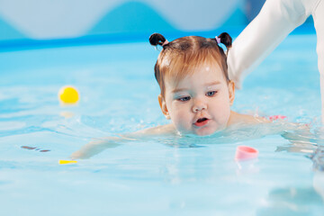 Fototapeta na wymiar Happy little baby girl swims in pool with trainer, concept development of muscles body and health care of kid