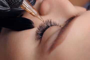 Closeup procedure permanent makeup tattoo eyeliner on eye of beautiful woman with black brows in...