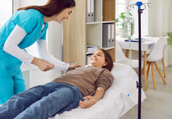Teenage child girl lying on the couch at office in clinic while doctor or nurse helping in...