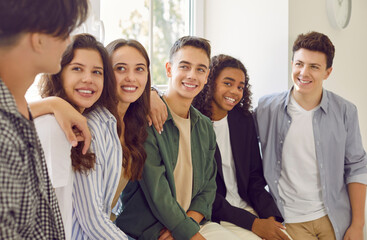 Portrait of a happy cheerful high school students in casual clothes standing together in hallway and friendly smiling to each other. Joyful diverse friends guys and girls talking indoors.