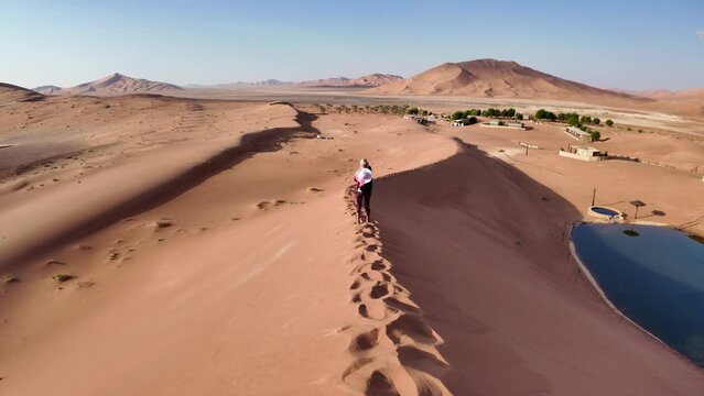 Woman photographer climbing the dunes of Empty Quarter Rub' al-Khali desert of Oman at sunset.