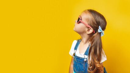 Portrait of a surprised cute little girl in sunglasses on a yellow background. Child model having...