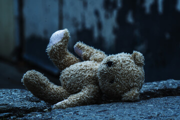 Conceptual image: Lost childhood, pain, hopeless and broken life concept. The teddy bear is lying down on the dirty asphalt