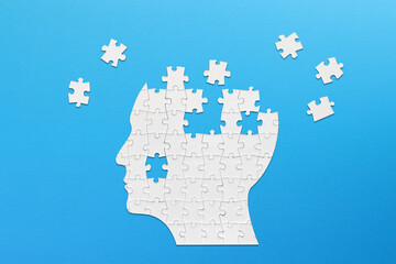 Brain shaped white jigsaw puzzle on blue background. Mental health and problems with memory.