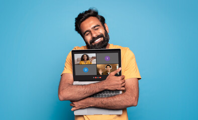 A contented man with a beard lovingly embraces his laptop, displaying a virtual meeting