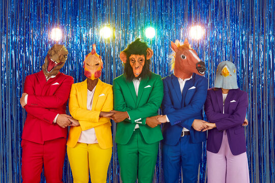 Multinational people dressed in bright costumes and rubber masks of different animals hold hands lined up for a photo shoot. Group of young friends in a club on a shiny blue background.