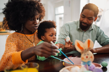 Multicultural family sits at home and coloring easter eggs on easter.
