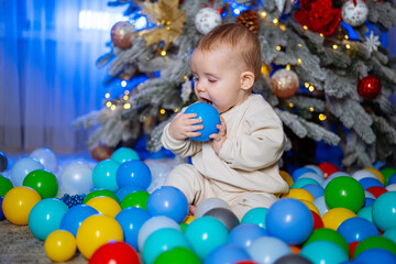 Fototapeta na wymiar Small child plays in ball pit under the Christmas tree.