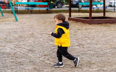 Little boy walks in the park in yellow vest and black pants
