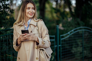 A trendy lady using her phone to call a taxi in a city next to a park.