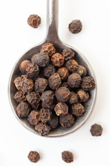 Black peppercorns in iron spoon on white background. Organic spice. Dry black pepper grain.