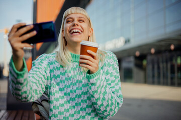 A young happy woman is laughing while having video call on a street.