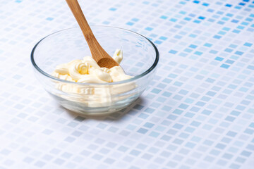 Glass bowl with mayonnaise and a wooden spoon.