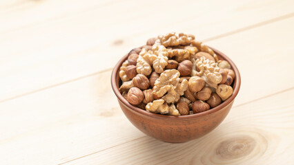 Mixed nuts in a clay cup on a wooden table, walnut kernels, peeled dried hazelnuts, almonds and cashews, top view, healthy and wholesome food concept.
