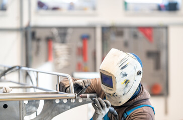 A helmeted man welds metal in a factory using personal protective equipment